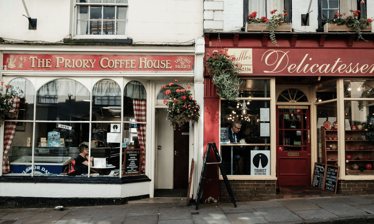 A picture of a British highstreet. On the left is The Priory Coffee House. On the right is a Delicatessen. This represents small and medium sized businesses.