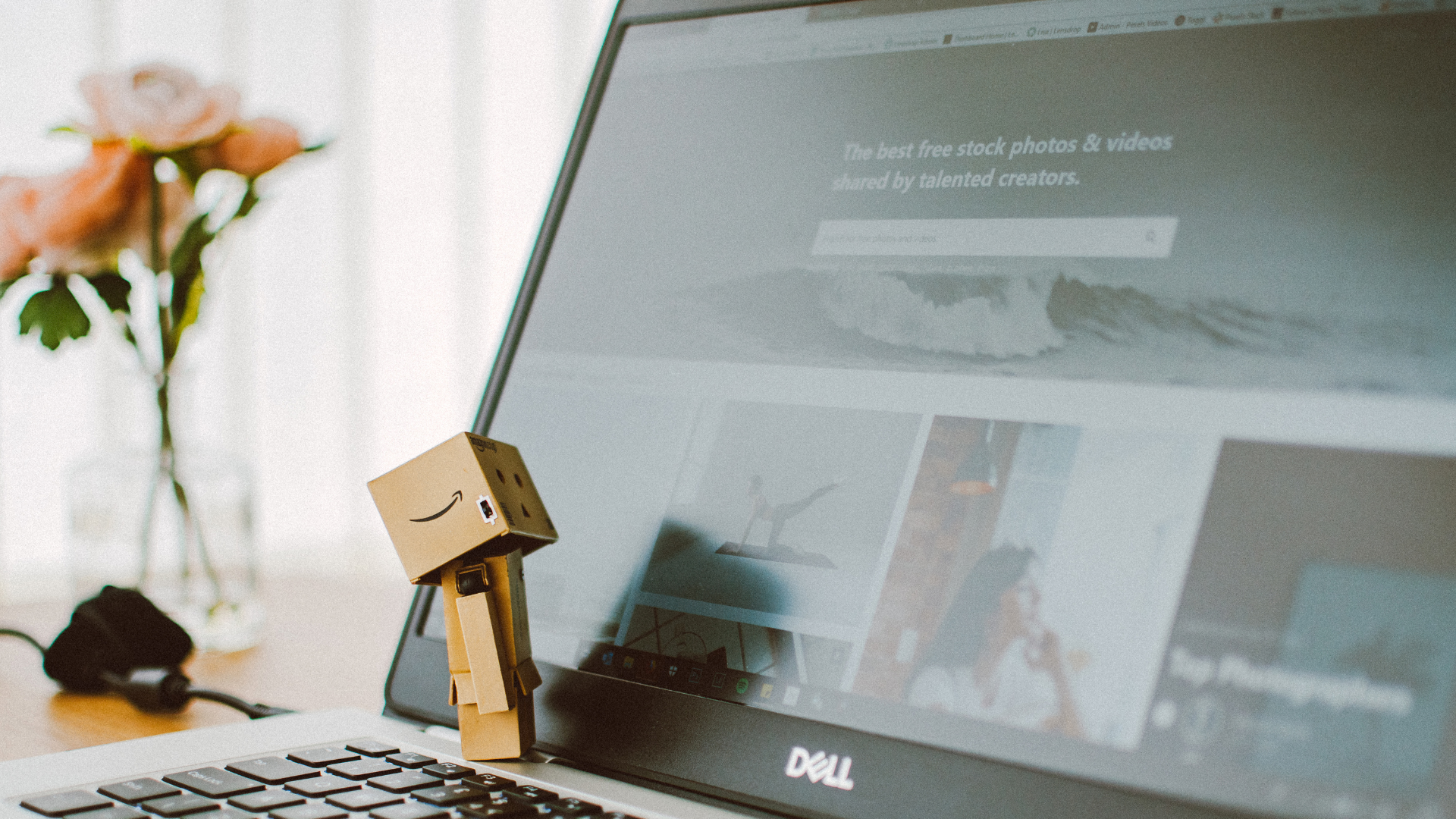 A small anamorphic pile of Amazon delivery boxes, representing a robot, sits on the keyboard of a laptop looking up at the screen. 